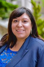 Headshot of Dr. Elizabeth Ramirez Arreola wearing a blue suit jacket over blue lace top. Sporting shoulder length straight brown hair with side swept bangs and a big smile. 