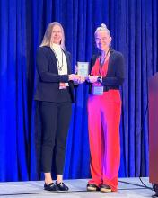 Dr. Amanda Lock Swarr receives the Bonnie & Vern L. Bullough Book Award, standing on stage with the award presenter, holding the plaque against a blue curtain backdrop