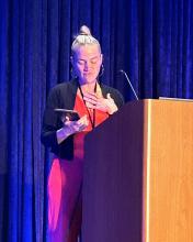 Dr. Amanda Lock Swarr stands at a podium, holding the Bonnie & Vern L. Bullough Book Award plaque with one hand while placing the other hand on her chest, appearing emotional during her acceptance speech.