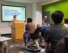 Marielle Marcaida presenting her project to a classroom of students. She is standing behind a lectern and on the screen behind her it reads: "Marielle Y. Marcaida, Department of Gender, Women & Sexuality Studies, PhD in Feminist Studies."