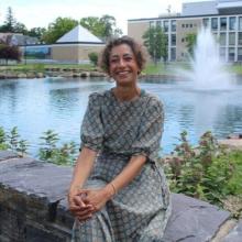 Dr. Akanksha Misra smiling while seated outdoors beside a pond and fountain on a university campus.