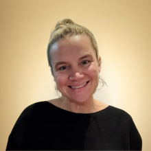 Headshot of Amanda Swarr, smiling, wearing a black sweater, against a gold background.