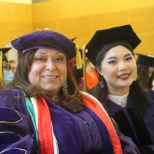 Upper body shot of two women wearing graduation gowns and caps and smiling at the camera