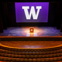 Meany Center stage with University of Washington's "W" block in white on the screen with a purple background