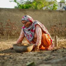 Indian woman crouched down collecting soil in a clay bowl