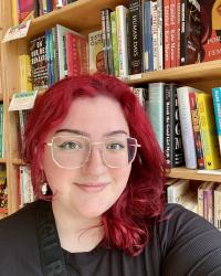 Woman with red hair stands in front of a bookshelf