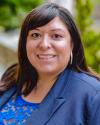 Headshot of Dr. Elizabeth Ramirez Arreola wearing a blue suit jacket over blue lace top. Sporting shoulder length straight brown hair with side swept bangs and a big smile. 