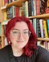 Woman with red hair stands in front of a bookshelf