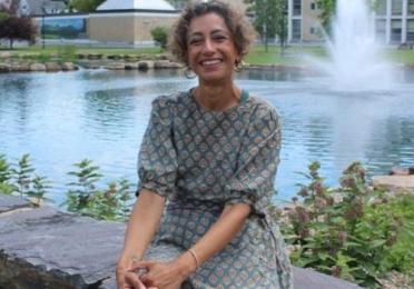 Dr. Akanksha Misra smiling while seated outdoors beside a pond and fountain on a university campus.