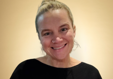 Headshot of Amanda Swarr, smiling, wearing a black sweater, against a gold background.