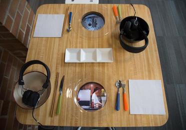 A wooden table set with headphones, colorful cutlery, napkins, and image plates. A condiment dish is centered on the table.