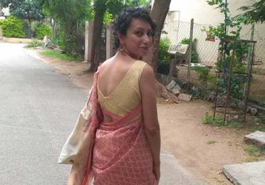 Akanksha Misra walking down a rural street, turning to face the camera over her shoulder.