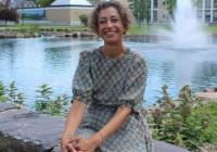 Dr. Akanksha Misra smiling while seated outdoors beside a pond and fountain on a university campus.