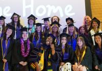 Students of the Class of 2026 stands and crouches for a group photo wearing their black graduation cap and gown in front of a projector screen