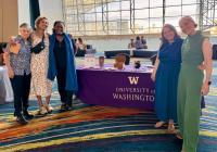 Five GWSS faculty, alumni, and friends stand smiling beside a University of Washington table at the NWSA conference.