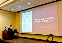 Petrus Liu presents at a podium in a lecture hall, standing beside a projected slide reading “The Value Turn in Queer Theory,” with his name, Boston University, and the date displayed.