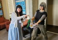 Liz and Sasha stand smiling holding the traditional GWSS Ph.D. sash with multiple years etched