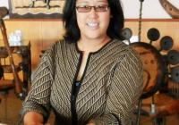 An upper-body shot of Professor Regina Lee, an asian woman wearing glasses with shoulder-length, dark brown hair, and wearing a button up cardigan with her hands folded on the table in front of her.
