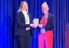 Dr. Amanda Lock Swarr receives the Bonnie & Vern L. Bullough Book Award, standing on stage with the award presenter, holding the plaque against a blue curtain backdrop