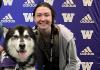 Hailey Capps crouched next to Dubs, an Alaskan Malamute, who is on a table to her right. They are in front of a purple backdrop covered in gold "W"s and the Adidas logo. 