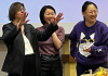 Nancy Kenney and two of her teaching assistants stand at the head of the classroom laughing. In front of them is a table with a bouquet of flowers