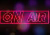 Hollow neon pink text reading "On Air" inside a pink box with blurry colorful dots in the background