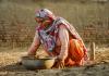 Indian woman crouched down collecting soil in a clay bowl