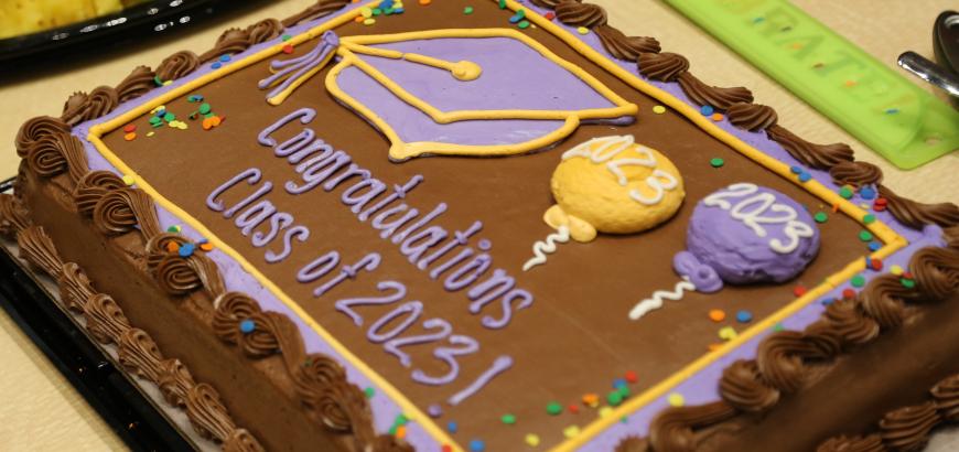 A chocolate sheet cake with the image of a graduation cap and balloons. Cake reads &quot;congratulations class of 2023!&quot;
