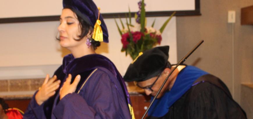 Profile image of Doctoral Recipient, Mediha Sorma, standing elegantly in full graduation regalia with hands on chest and eyes closed as Doctoral Committee Chair, Professor Chandan Reddy, stands behind her adjusting the hood he has just placed over her head.