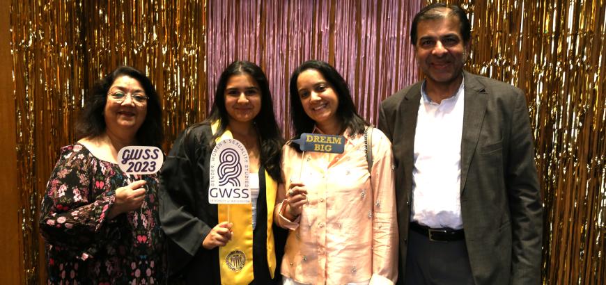 A young woman in a graduation gown posing for a photo with three family members, including her parents. They are holding up paper signs: the GWSS logo, &quot;GWSS 2023,&quot; and &quot;Dream Big.&quot; with the