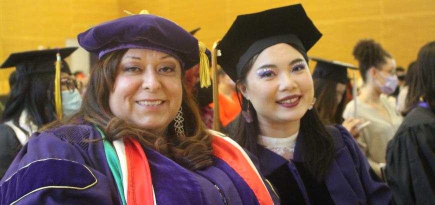 GWSS Ph.D. students, Elizabeth Ramirez Arreola and Yingyi Wang, pictured from middle up wearing graduation gowns and smiling at the camera