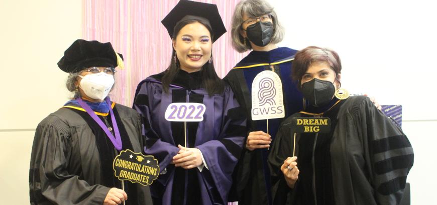A group of four standing under a gold congrats banner. All are wearing graduation robes and holding signs, including &quot;congratulations graduates,&quot; &quot;2022,&quot; the GWSS logo, and &quot;dream big&quot;