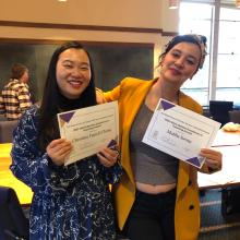 Christina Yuen Zi Chung and Mediha Sorma smiling at camera with arms around each other while holding up copies of their Marie Doman Award certificates