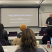 Eric Villiers standing behind a podium in front of a classroom of students. On the screen behind him, the title of his presentation, "Falling Asleep in the Museum"